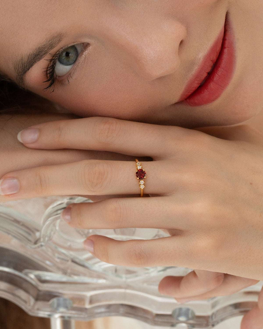 Gold garnet five-stone ring worn on finger, showing red center and clear side stones
