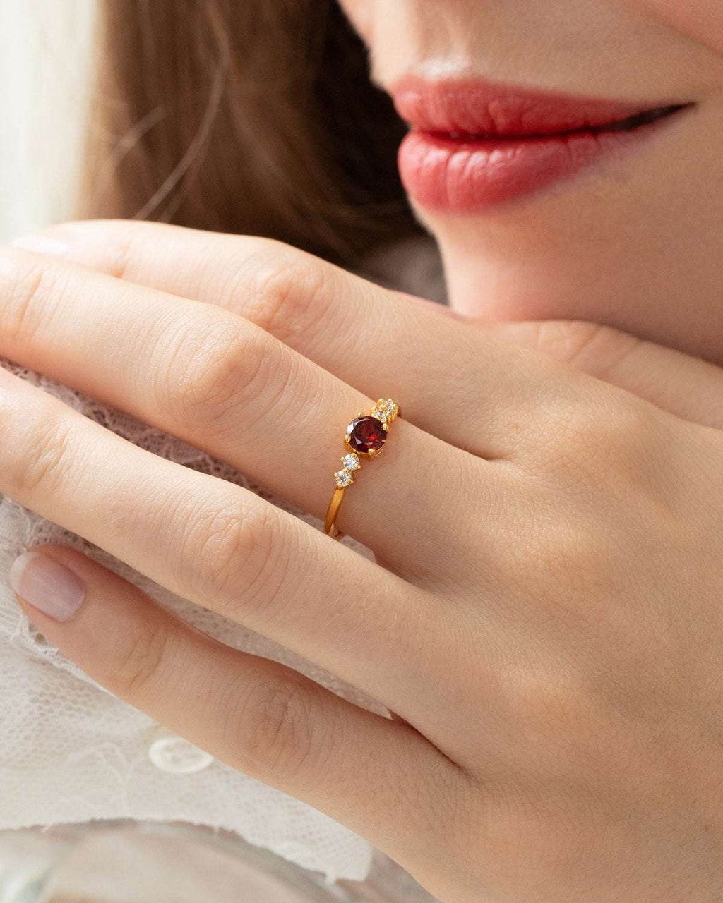 Garnet ring on finger: round red center stone with small clear side stones in gold
