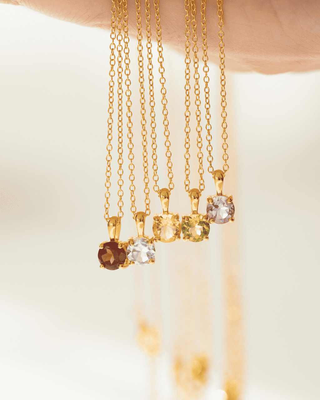 Assorted gold solitaire pendant necklaces with faceted gemstones hanging on chains