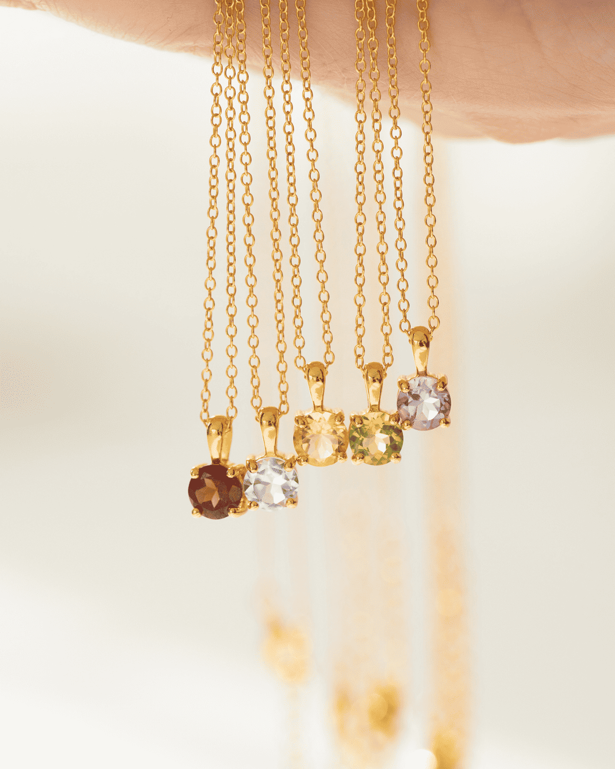Assorted gold solitaire pendant necklaces with faceted gemstones hanging on chains