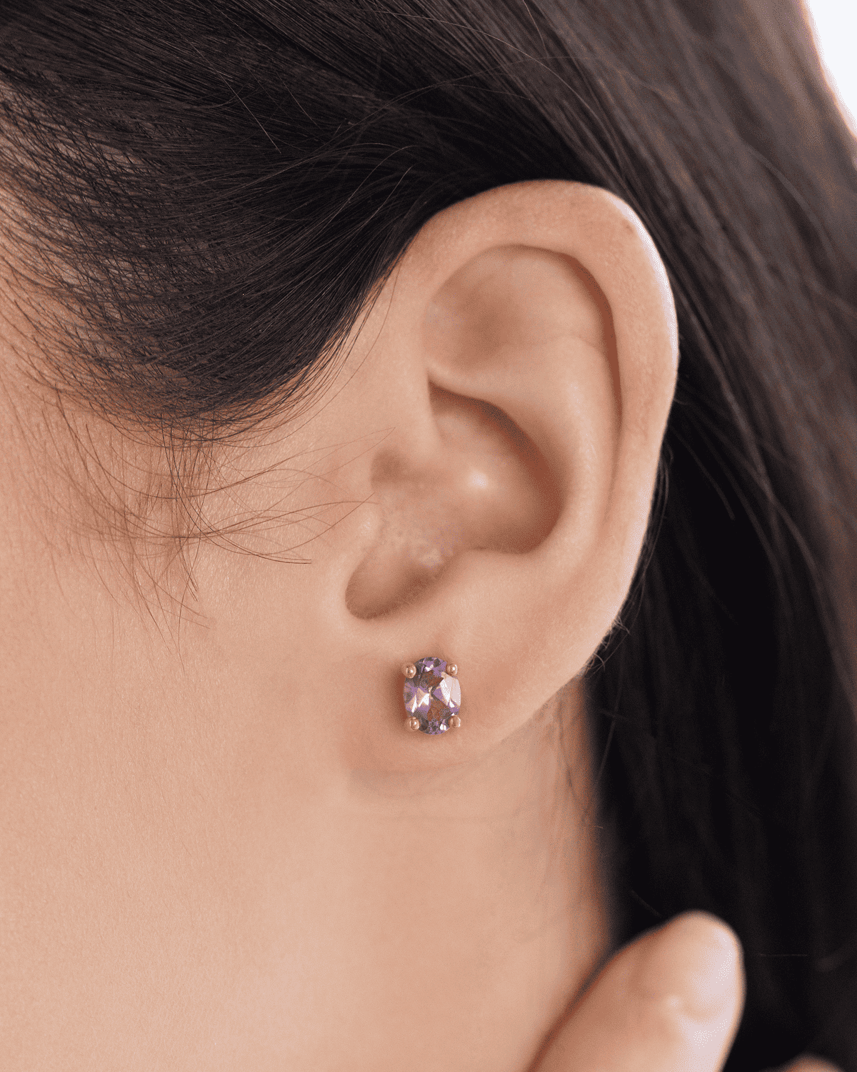 Gold stud earring with purple gemstone on model ear.