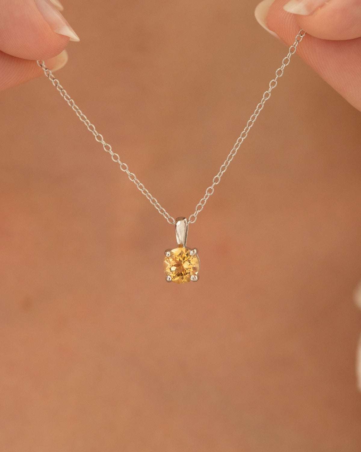 Sterling silver chain necklace with small round yellow citrine solitaire pendant, worn