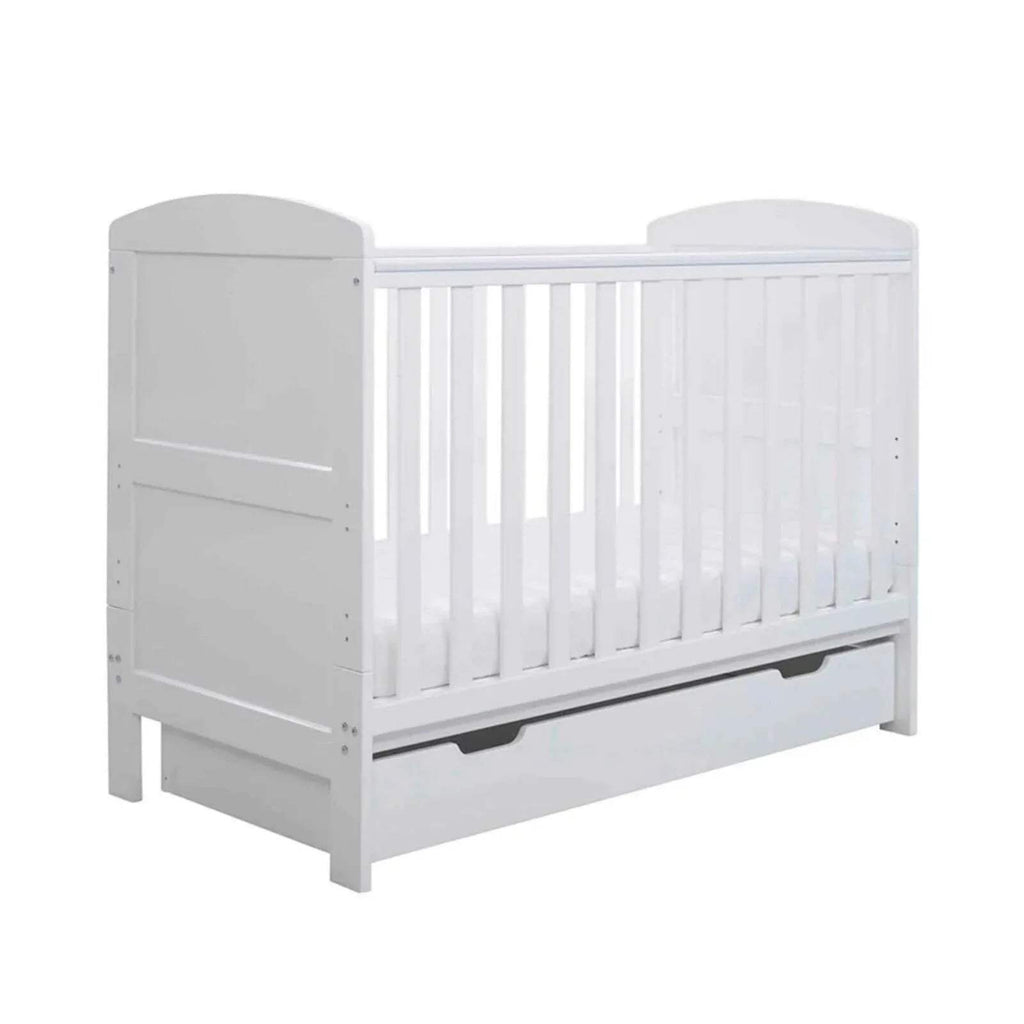 White mini cot bed with vertical bars and under-drawer panel, front-left view