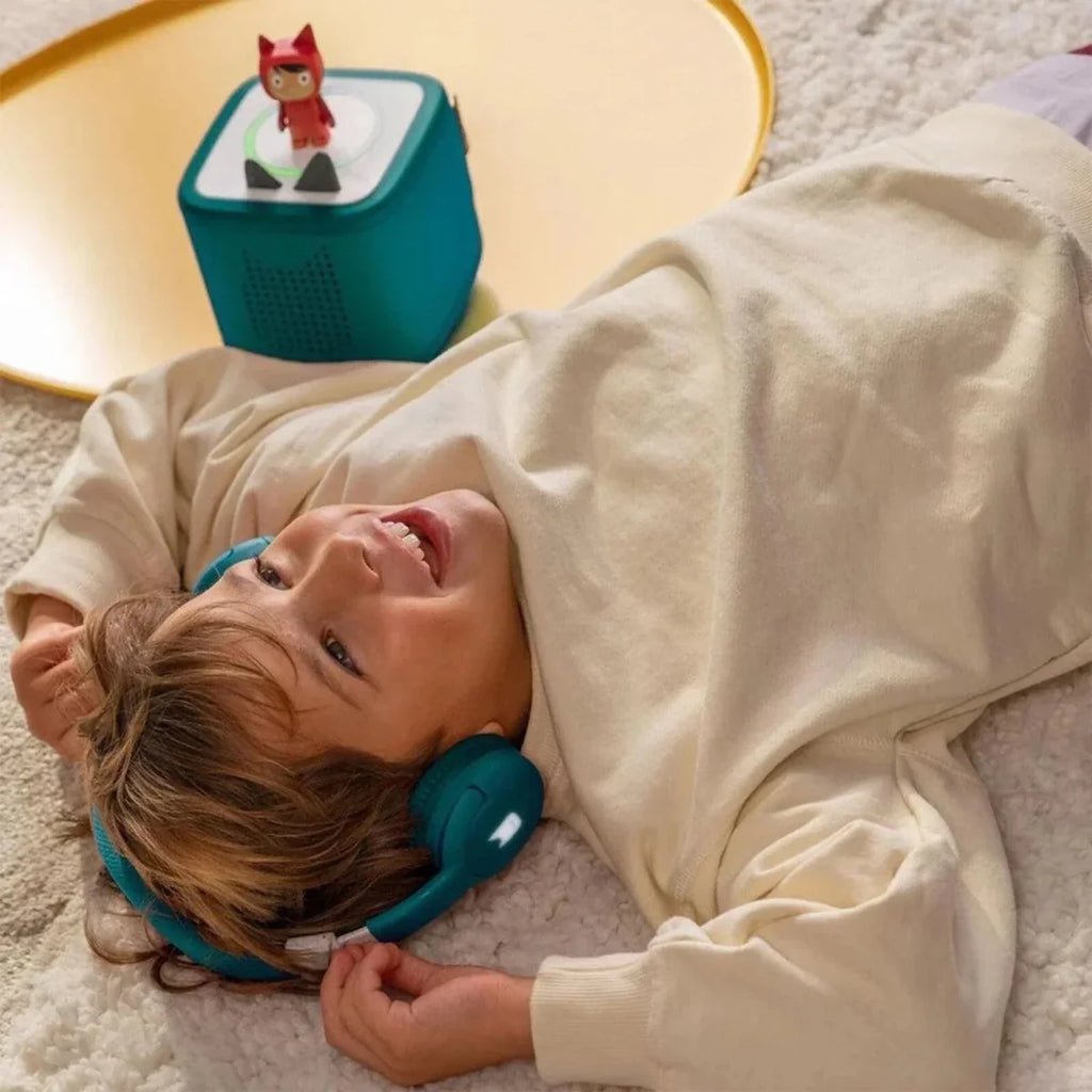 Child wearing teal headphones, with Toniebox 2 audio player nearby