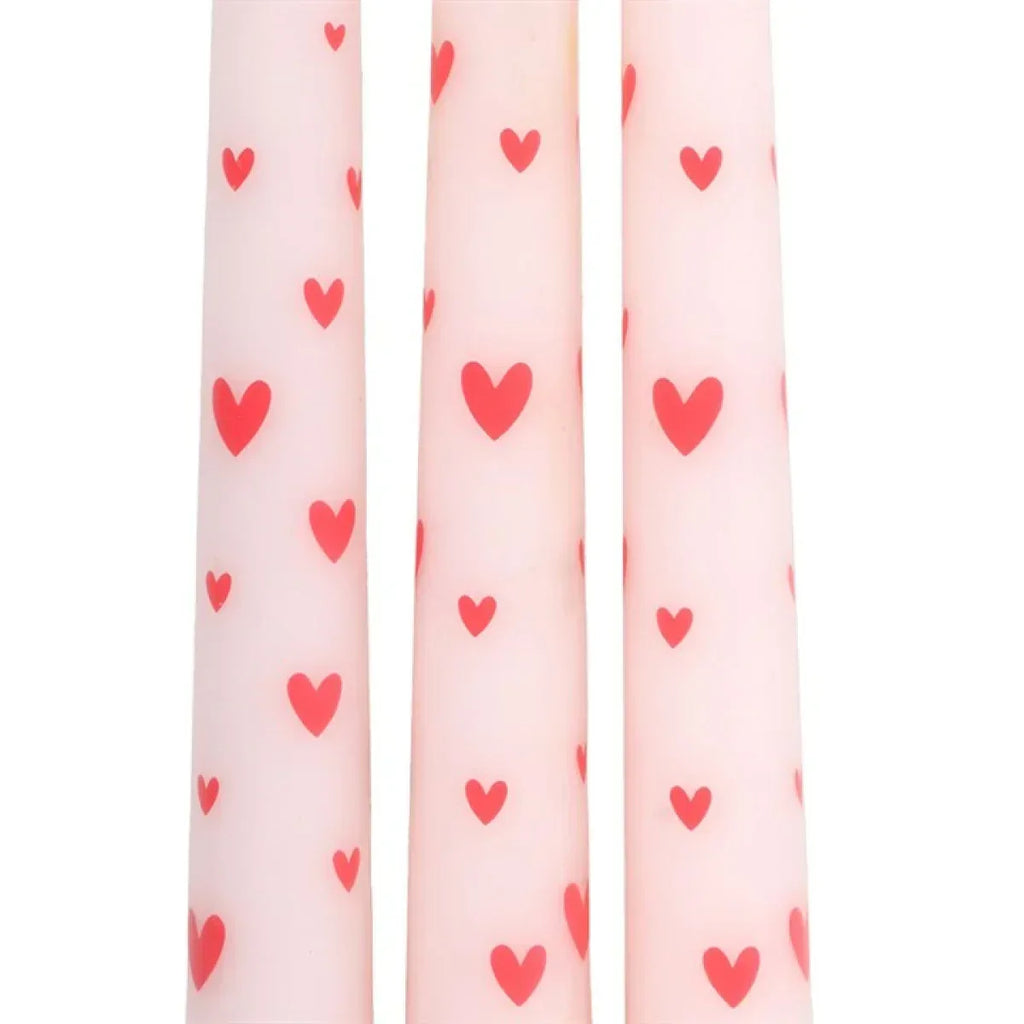 Close-up of three pink taper candles with red heart motifs