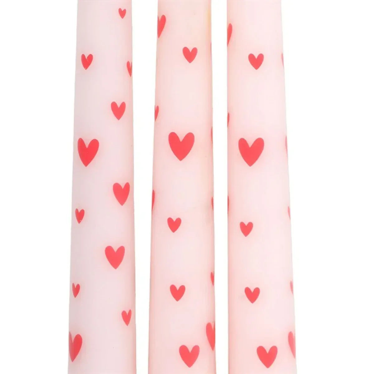 Close-up of three pink taper candles with red heart motifs