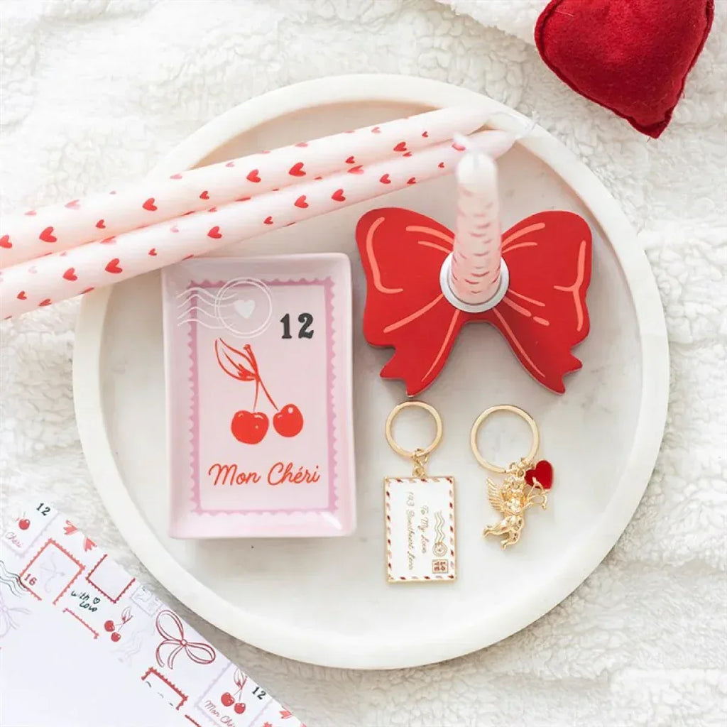 Pink square trinket dish with cherry stamp design, holding gold keychains and hearts