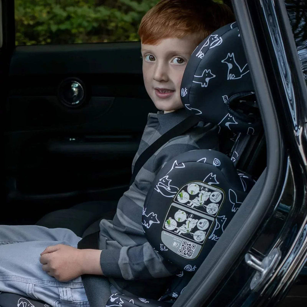 Black kids car seat with white cartoon print, boy wearing seatbelt