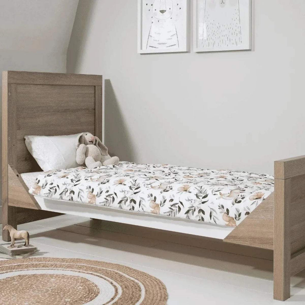 Oak toddler bed with slatted headboard and fitted floral mattress cover