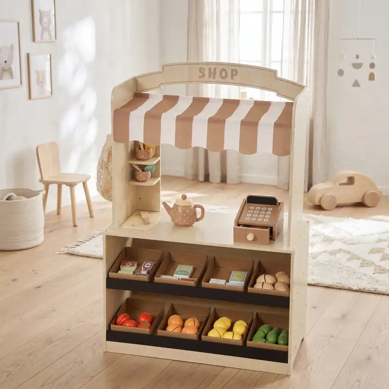 Wooden kids play shop with striped awning, cash register, and neatly arranged toy groceries
