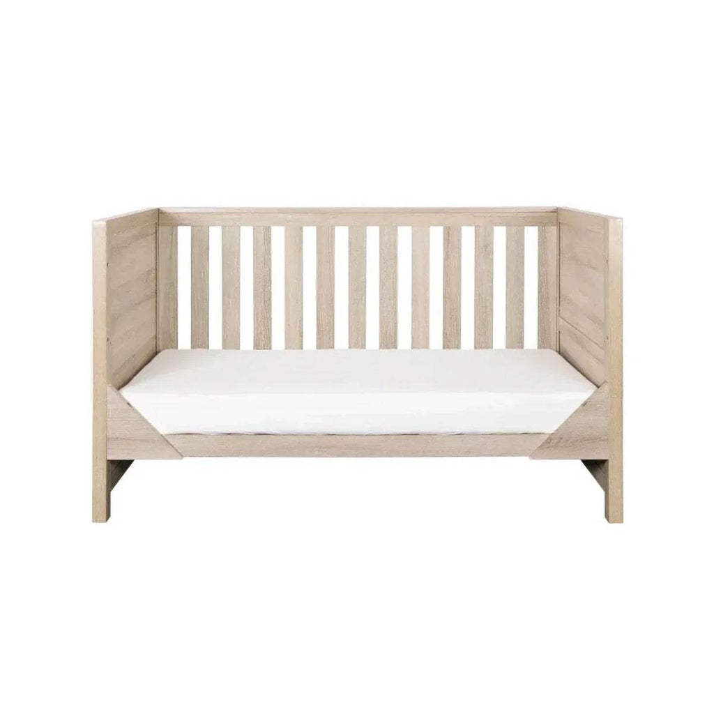 Oak cot bed with solid end panels, vertical slat headboard and footboard, and mattress platform