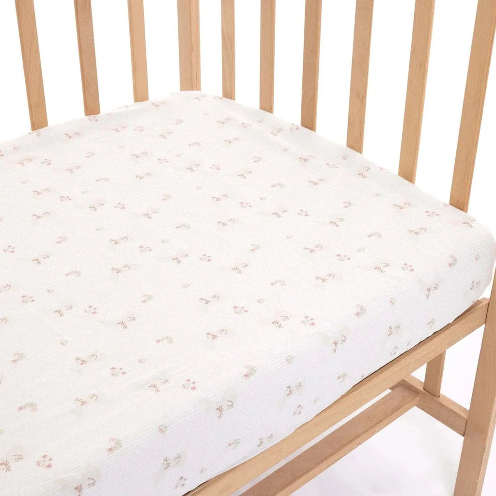 White baby fitted sheet on a crib, with small pastel floral print