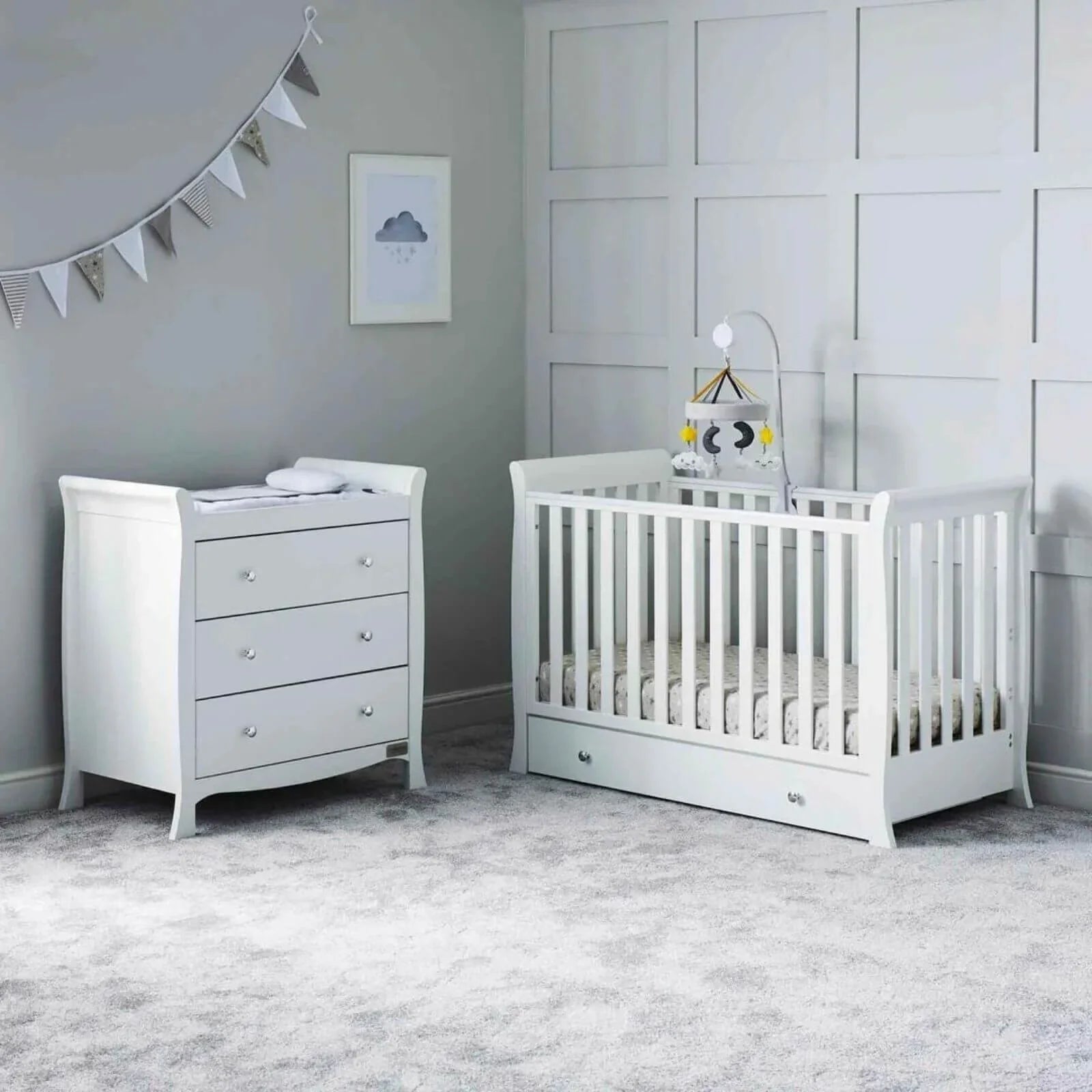 White mini cot beside matching dresser in a nursery setting