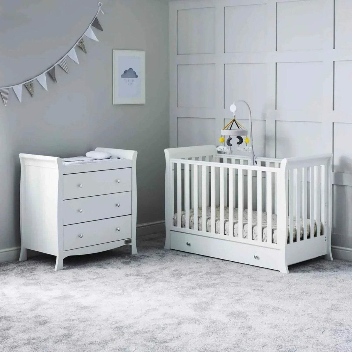 White baby crib with drawer base and matching dresser in nursery setting