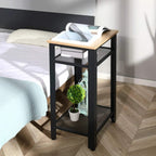 Black side table with oak top and two wire-mesh shelves beside a bed