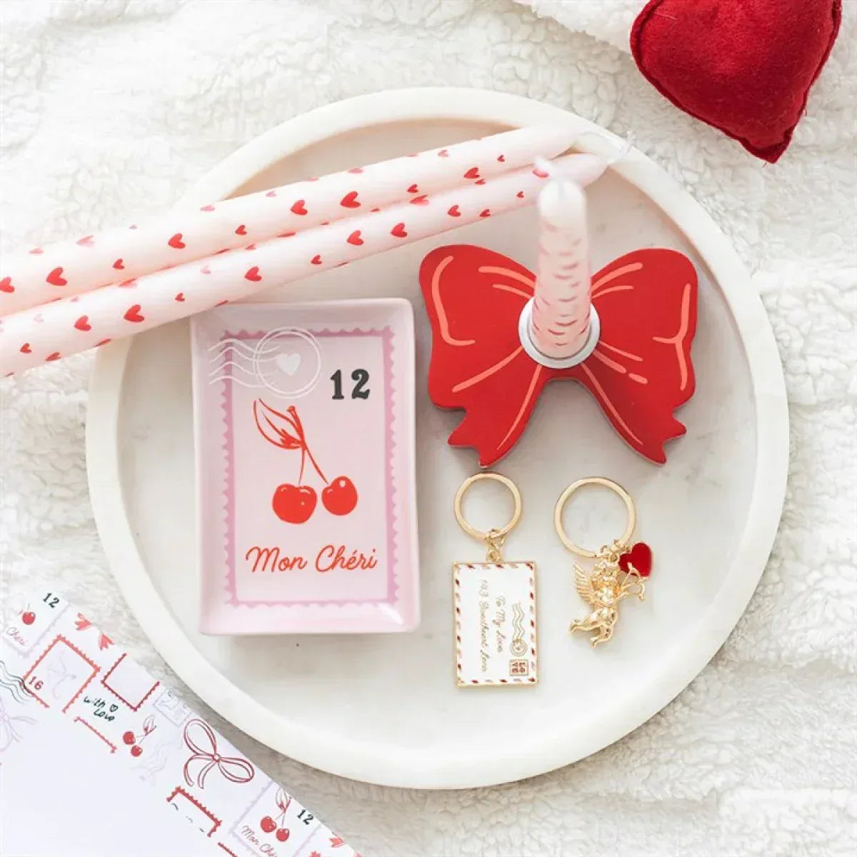 Pink taper candles with red hearts, rolled and displayed in a dish