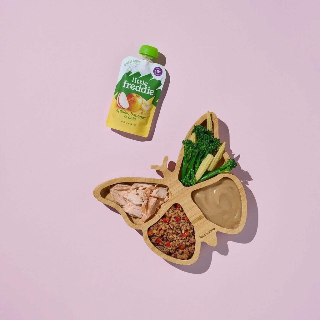 Little Freddie baby food pouch beside wooden bowls of fruit, oats, and greens