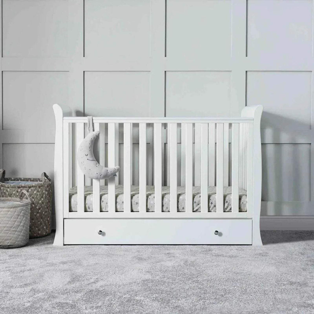 White baby crib with slatted rails and drawer front panel