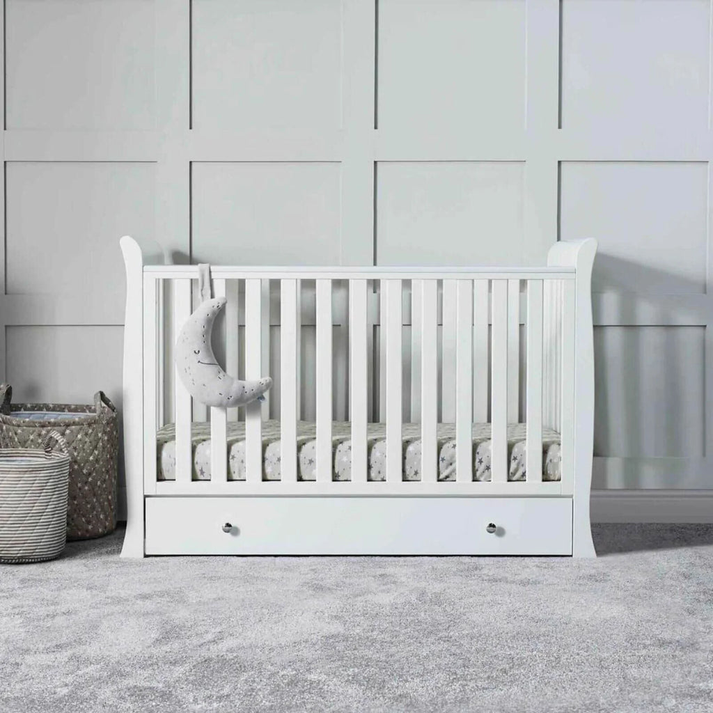 White mini cot bed with front drawer, bed rails, and striped fitted mattress