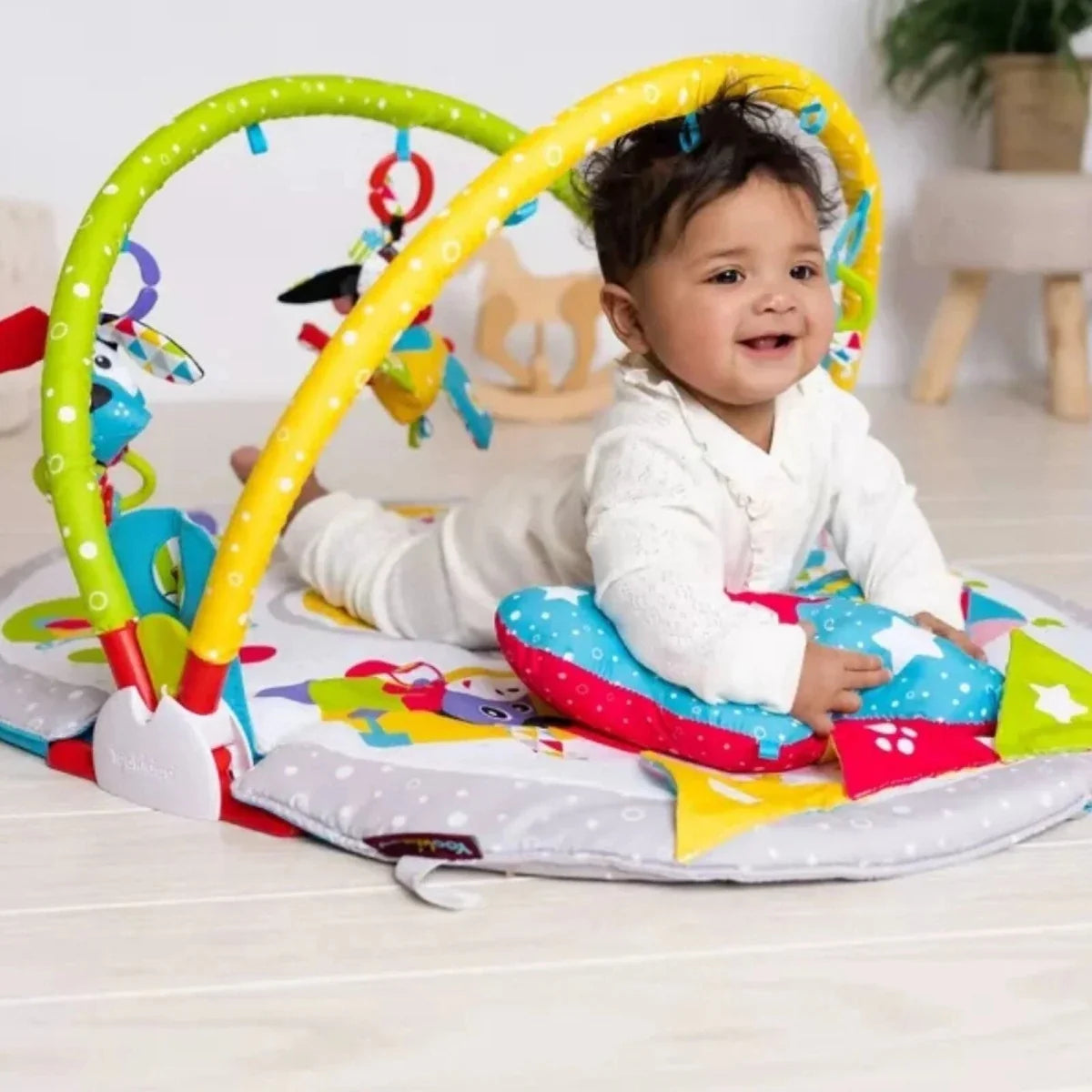 Baby sitting on colorful play gym mat with hanging animal toys under arches