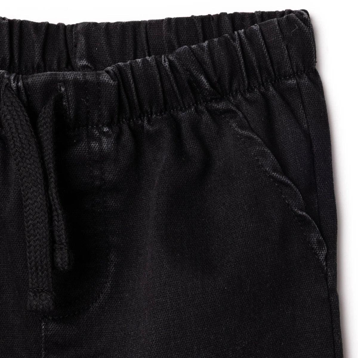Black denim trousers close-up: front pocket detail and fly stitching