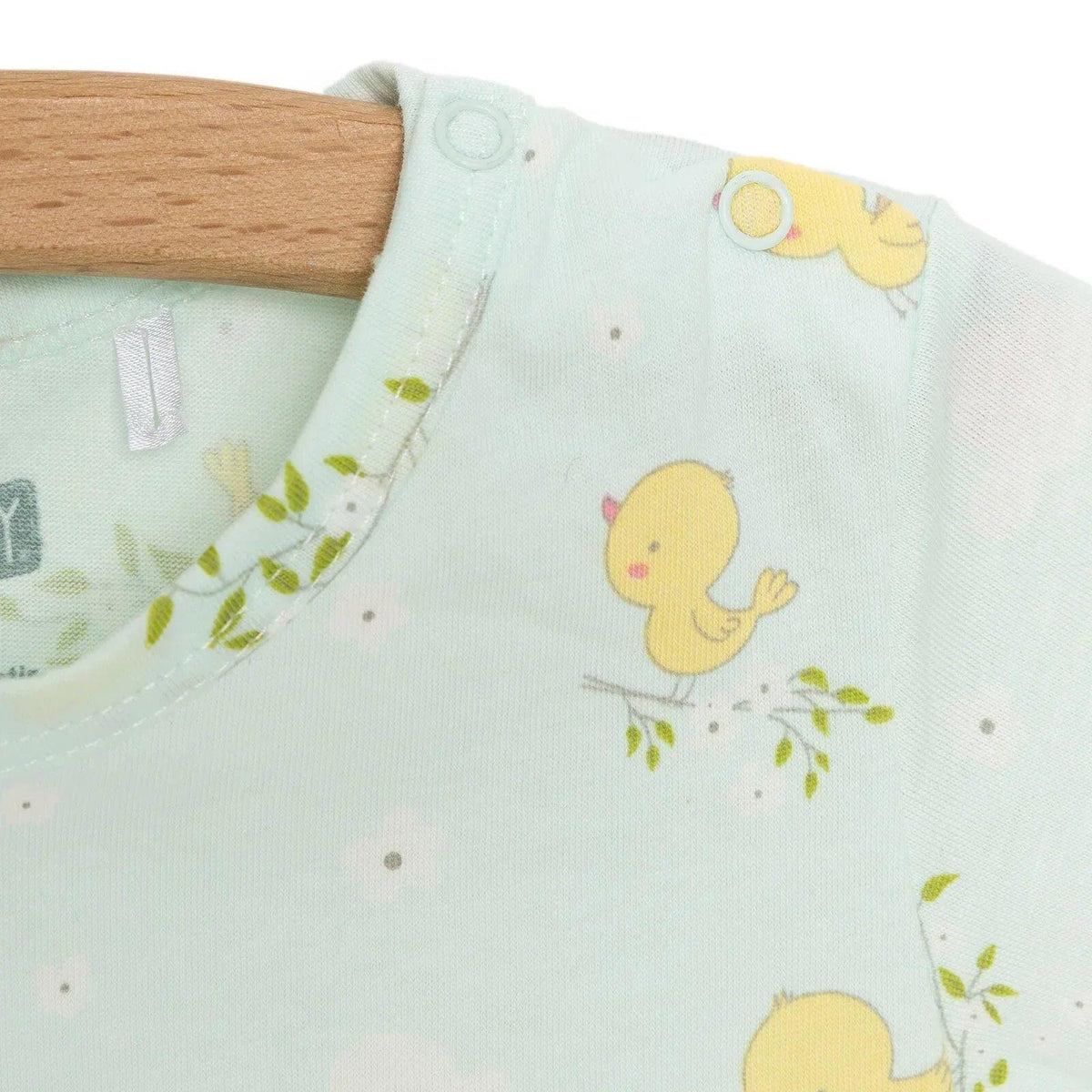 Light blue baby romper chest close-up with yellow chick graphic and snap button at shoulder