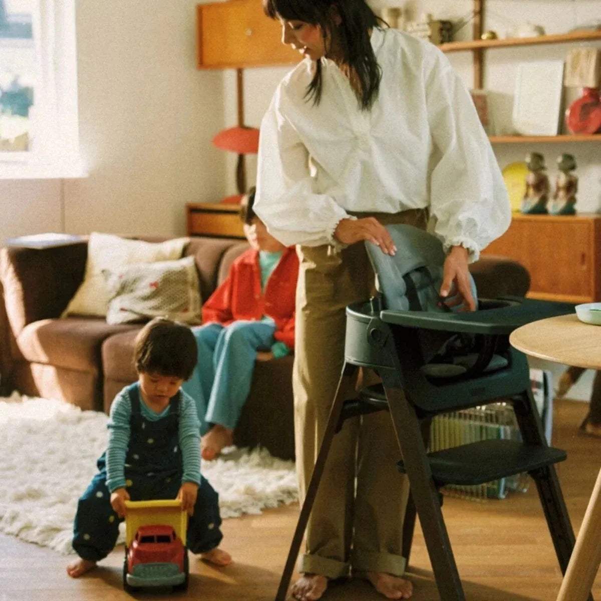Stokke Steps highchair with dark frame and tray, next to a low play area
