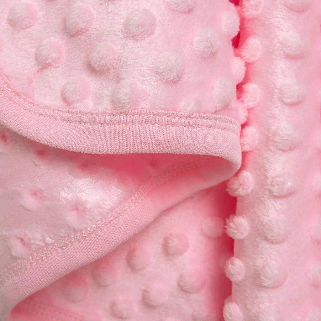 Pink fleece baby blanket seam detail with stitched hem and raised dot surface.