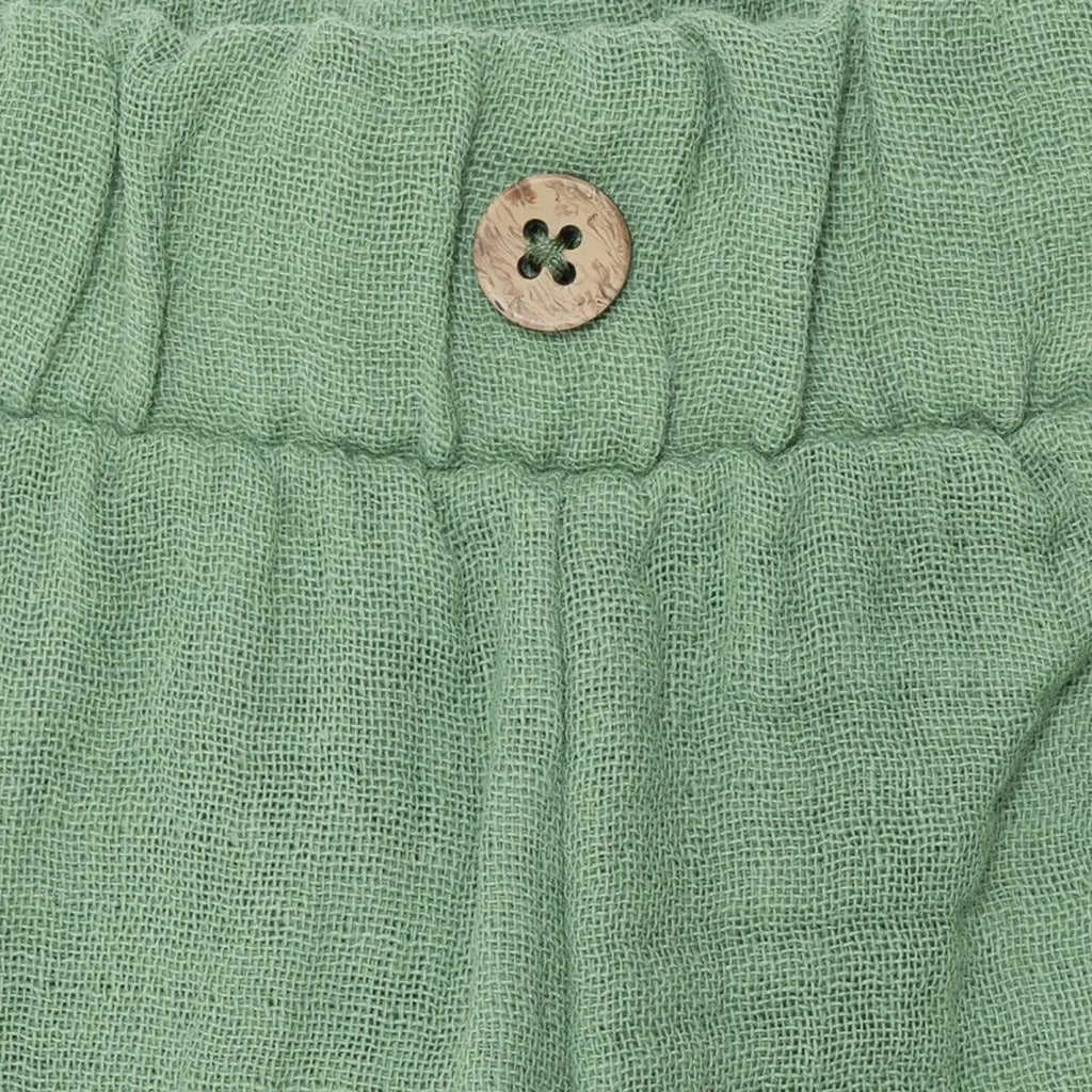 Elastic waistband button detail on green muslin baby shorts