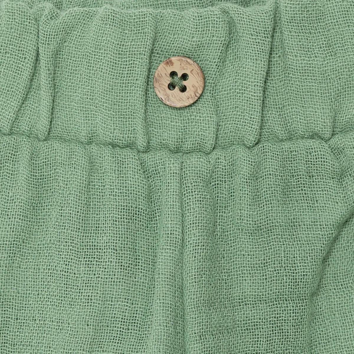 Elastic waistband button detail on green muslin baby shorts