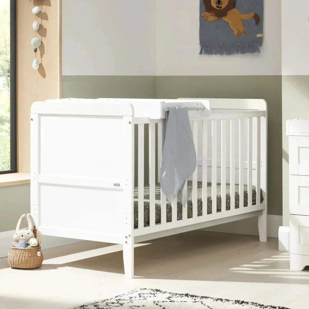 White cot bed with teething rail and side drawer front, styled for nursery use