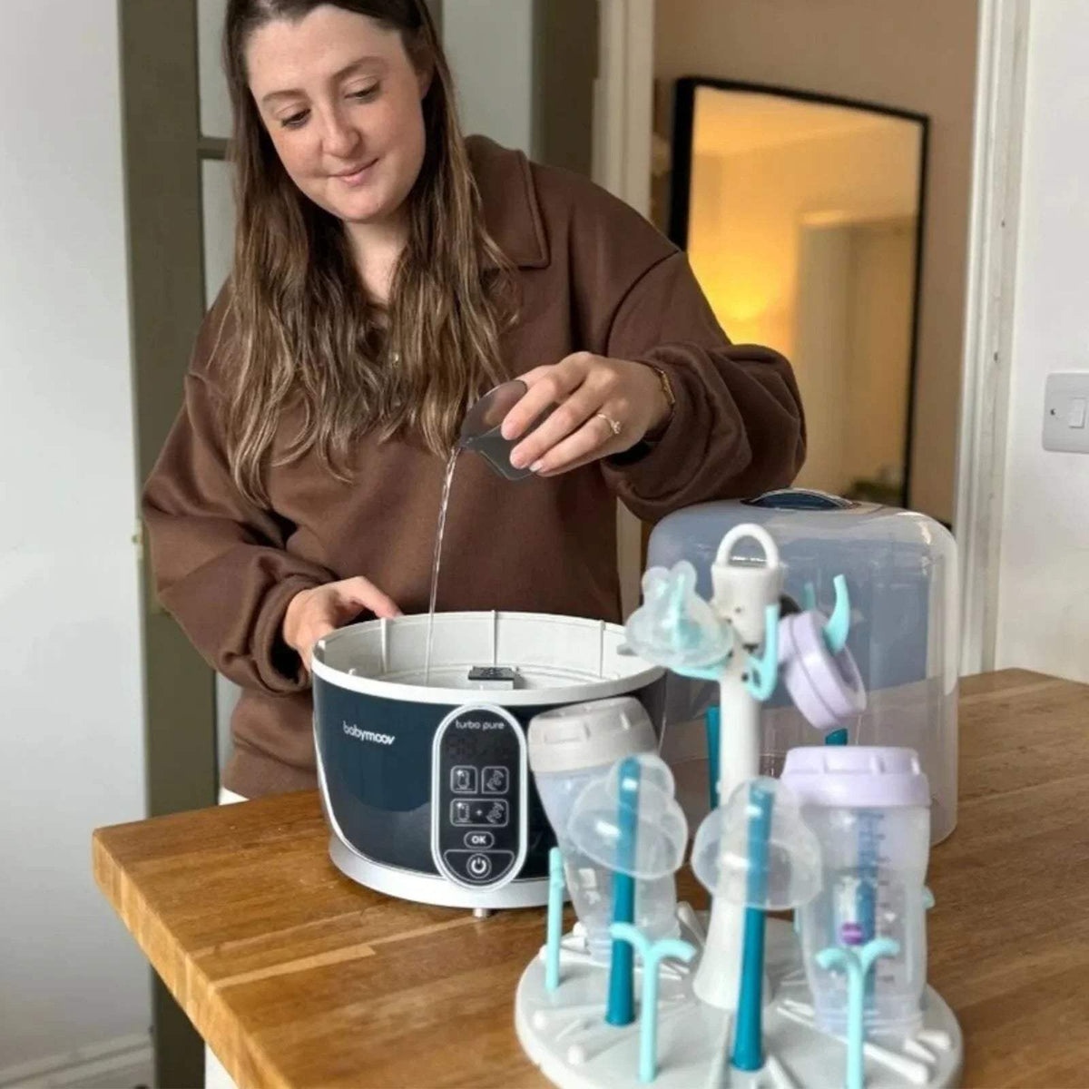 Babymoov Turbo Pure steriliser and dryer with bottle rack and lid, shown in use