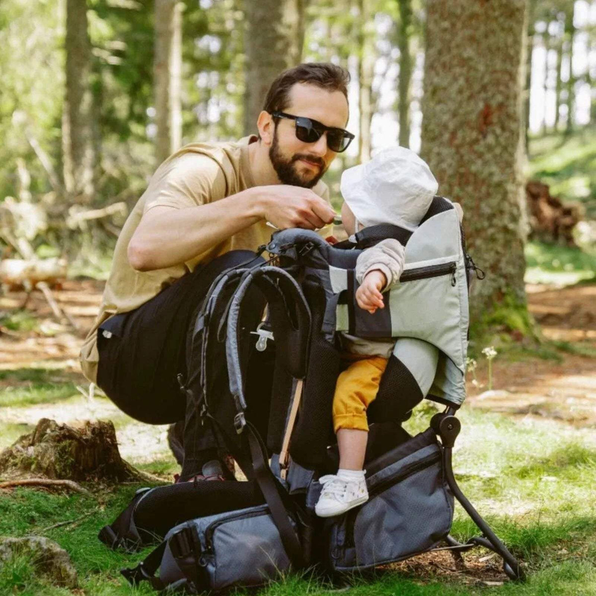Sage green baby carrier with canopy and seated child in the padded harness