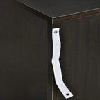 Anti-tip strap detail on dark cabinet corner with white fabric and metal anchor points.