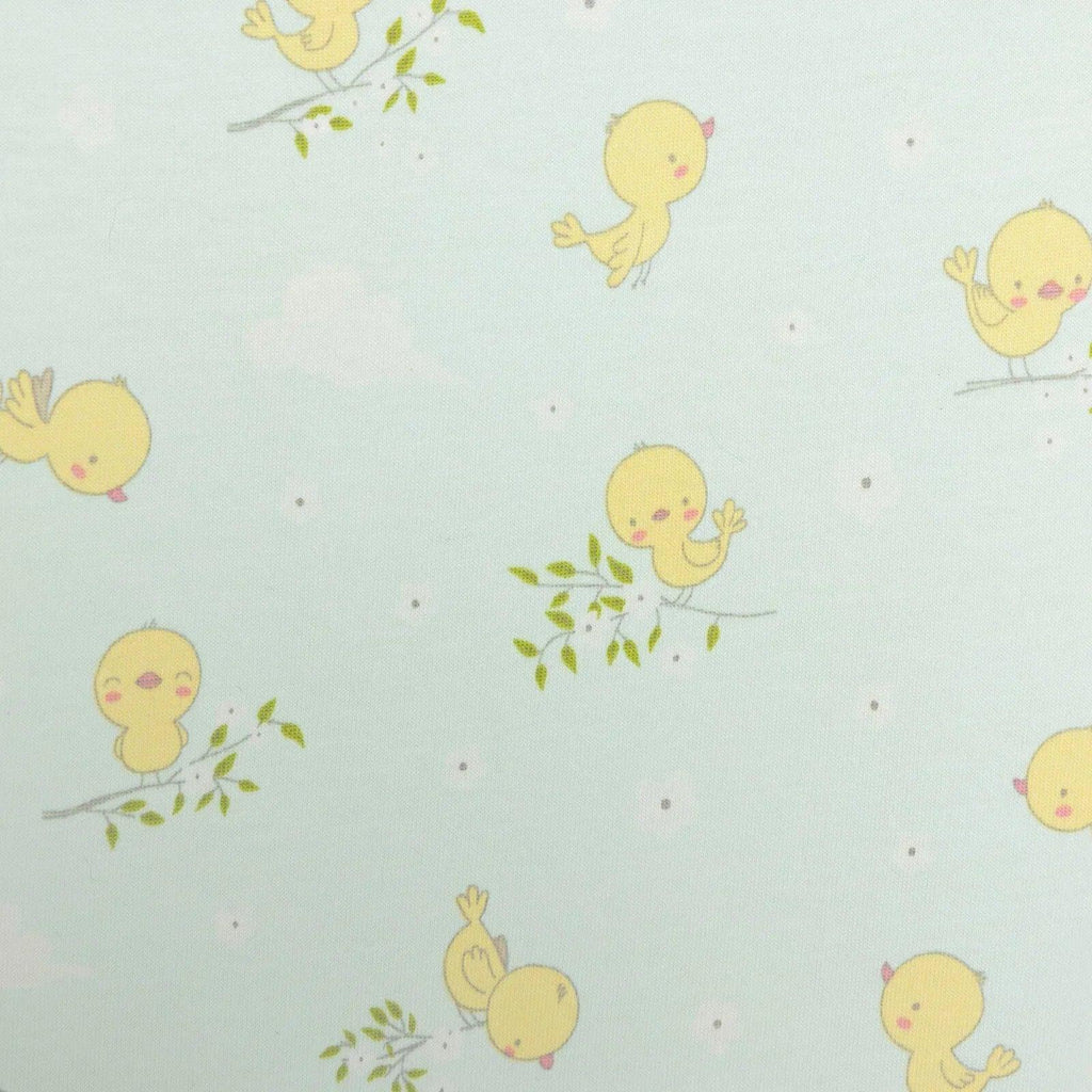 Light blue romper fabric close-up showing repeating yellow chick characters and green sprigs