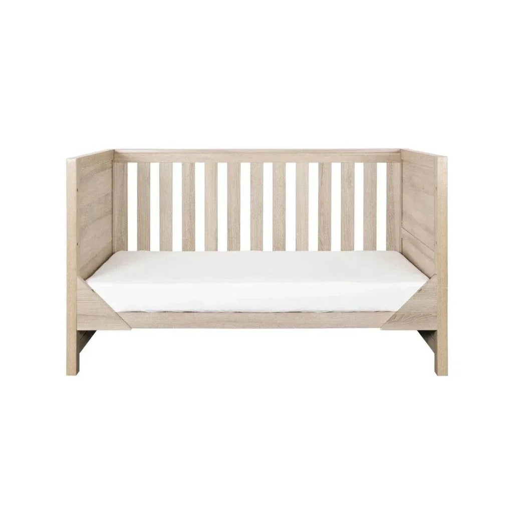 Oak cot bed with white mattress and vertical safety slats
