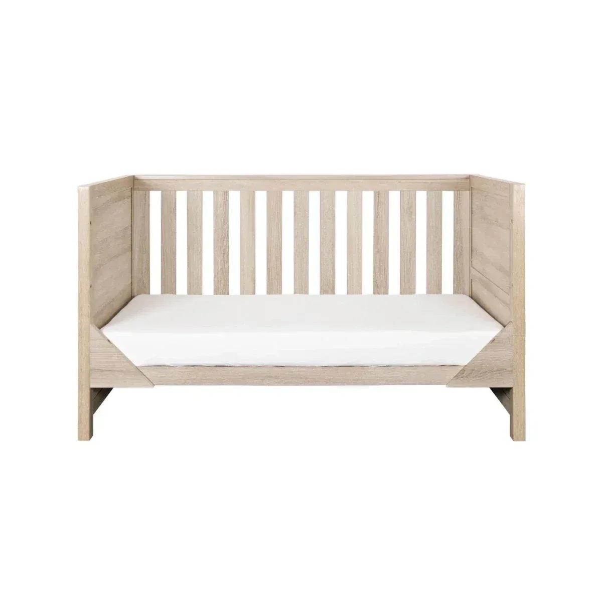 Oak cot bed with white mattress and vertical safety slats