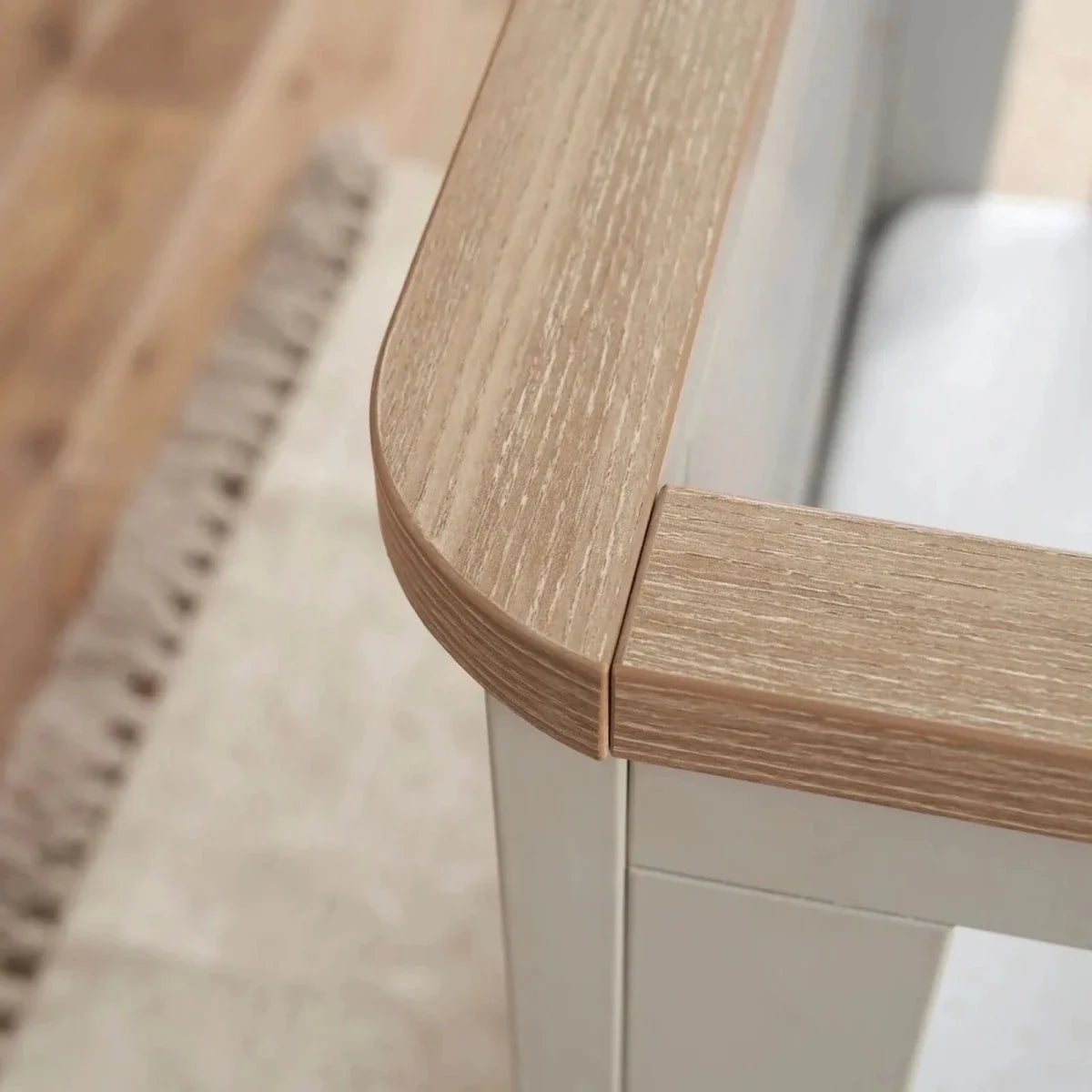 Close-up of curved oak-toned top rail on white cot bed with vertical slats