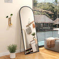 Black arched standing mirror tilted slightly, reflecting the room from the side