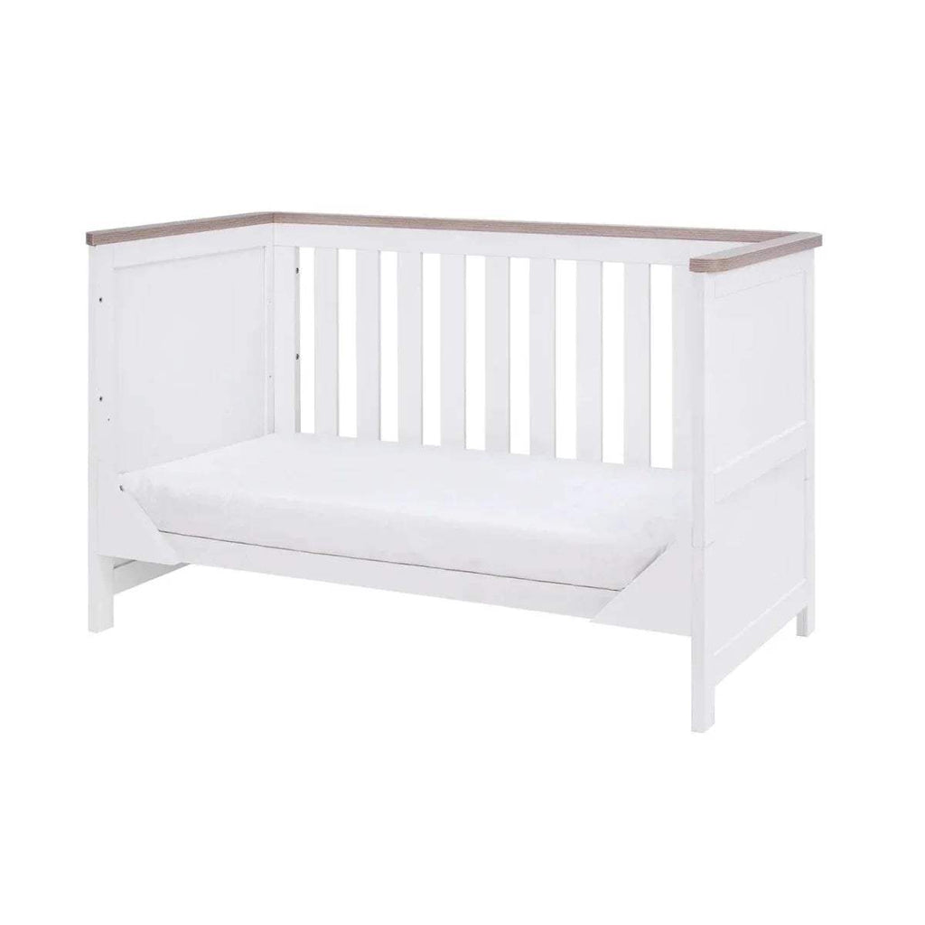 White baby cot with vertical slat sides, oak-toned top rail, and padded mattress base