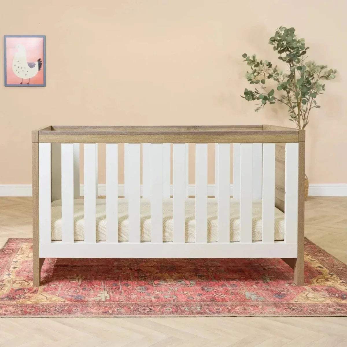 Light oak cot bed with white vertical slats and solid rails, front view.