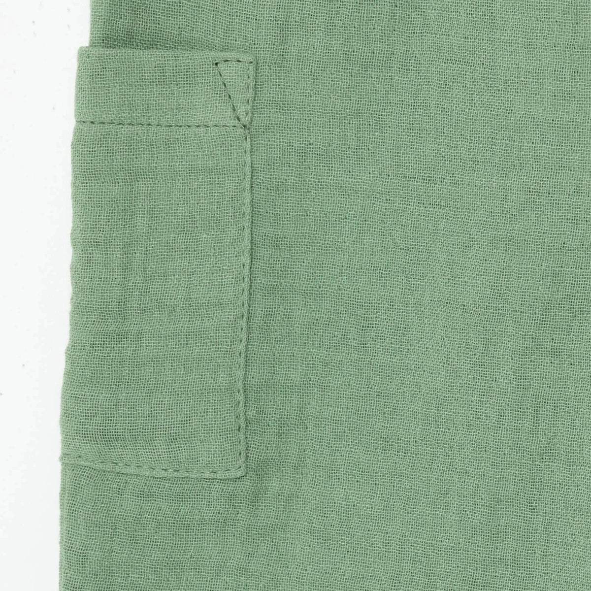 Green muslin baby shorts patch pocket close-up with stitched corners