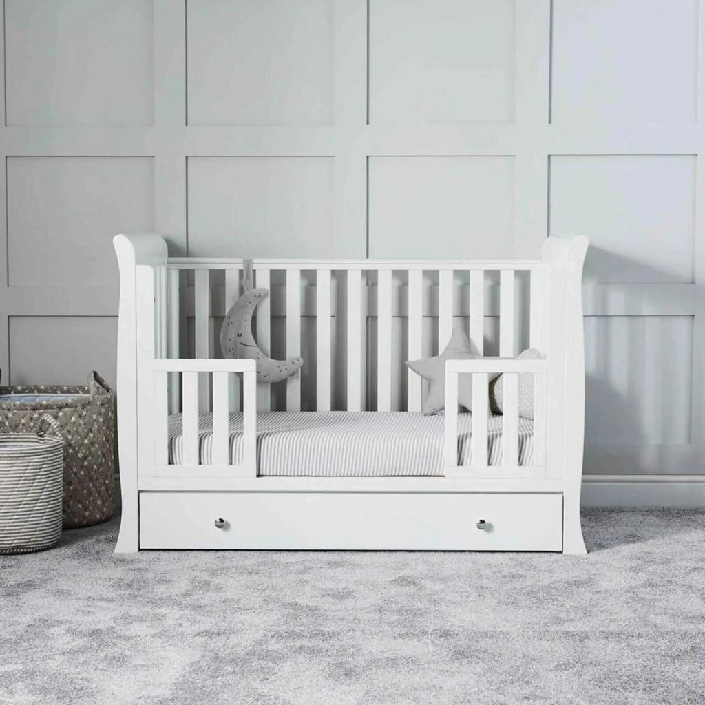 White mini cot with striped mattress and front drawer