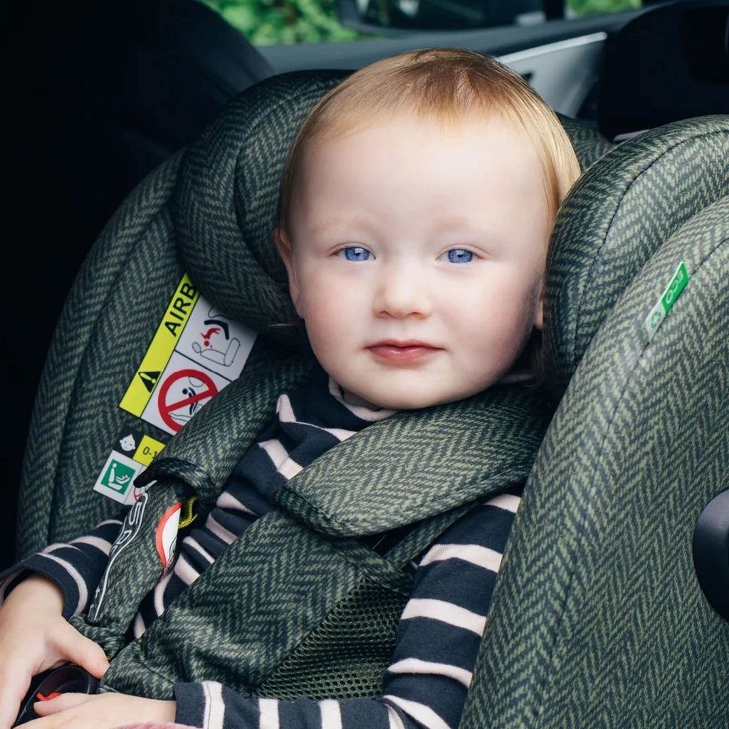 Baby in green Cosatto car seat with striped harness cover and patterned padding