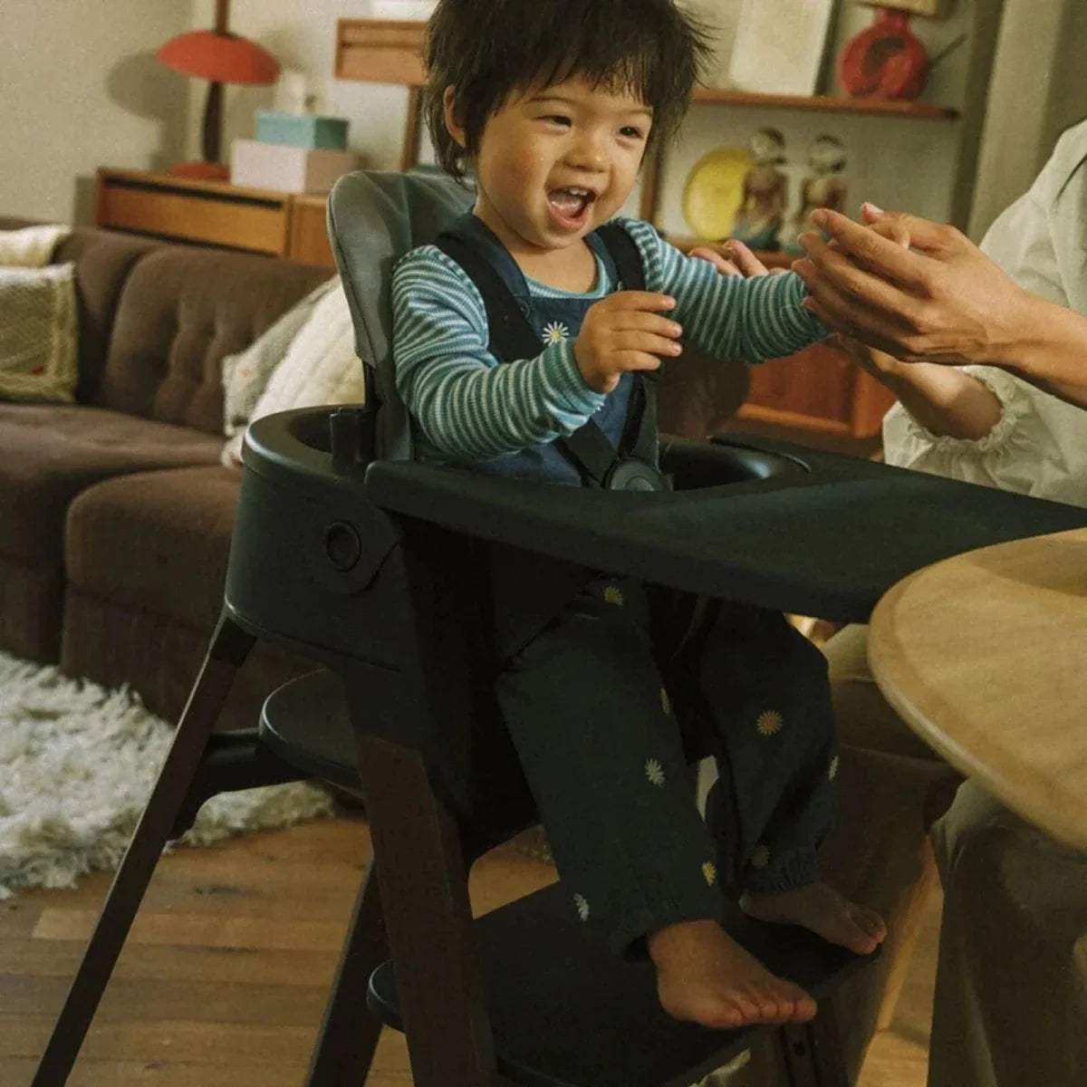 Black highchair with child seated, warm brown legs, and rounded tray