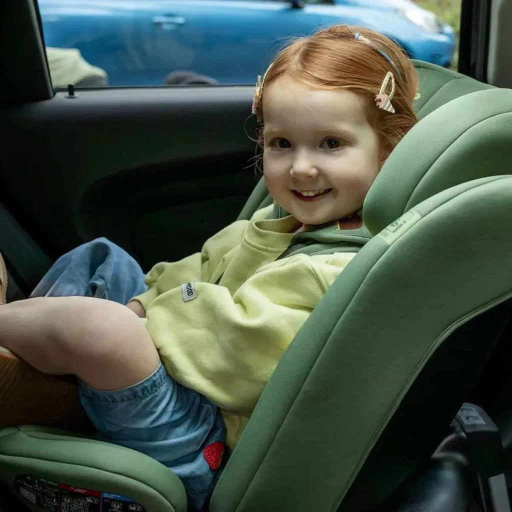 Green child car seat with padded harness, featuring a smiling child in the seat