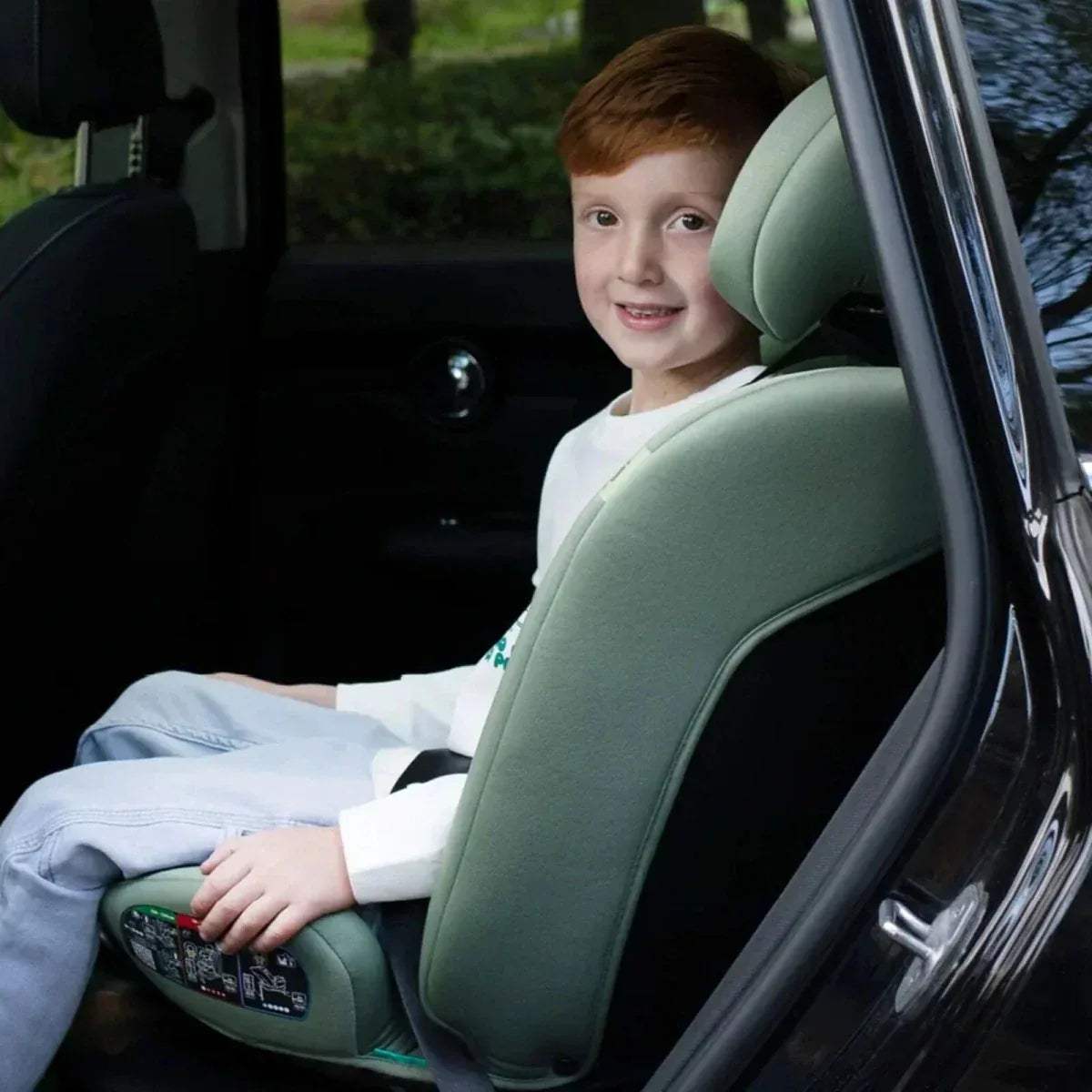 Child in green car seat, reclined with visible harness straps.