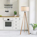 Beige fabric floor lamp shade on light wood tripod legs with black cable and plug