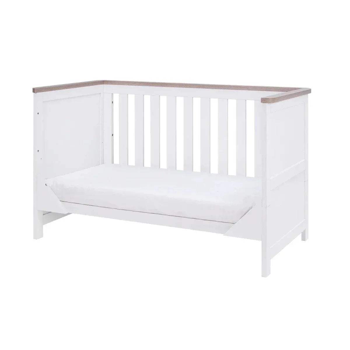 White cot bed with slatted rails and oak top trim, with a white mattress