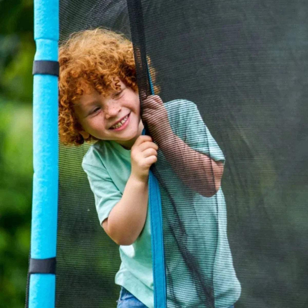 Child smiling behind trampoline mesh net with blue vertical pole